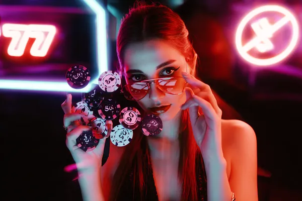 নিয়ন আলোয় আলোকিত পরিবেশে ক্যাসিনো চিপ হাতে এক অভিজাত নারী—যা CROWNBF–এর প্রিমিয়াম অনলাইন ক্যাসিনো পরিবেশকে তুলে ধরে।